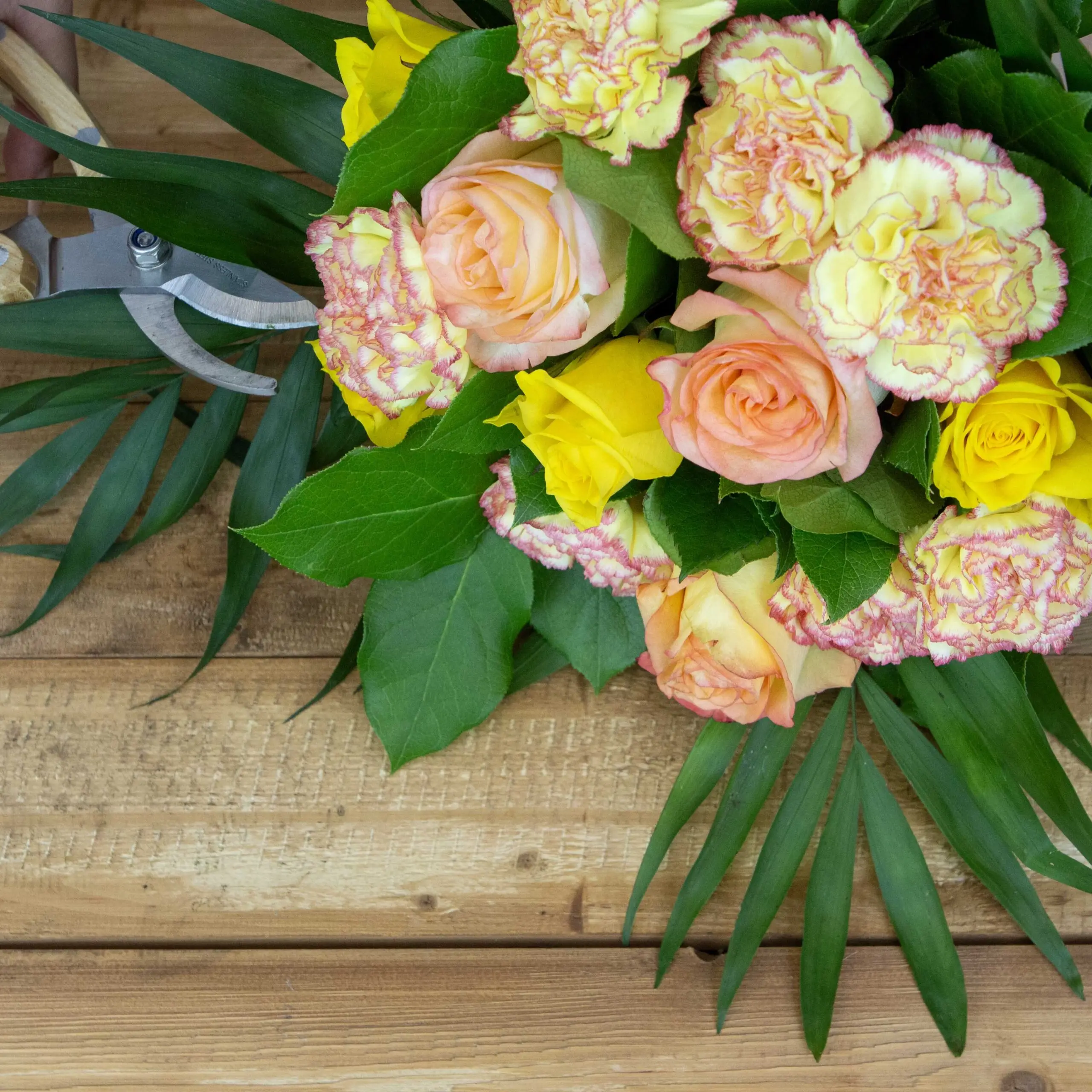 Bouquet Éclat de Soleil : roses oranges, roses jaunes, oeillets bicolore jaune/orangé, botte de sallal, chico
