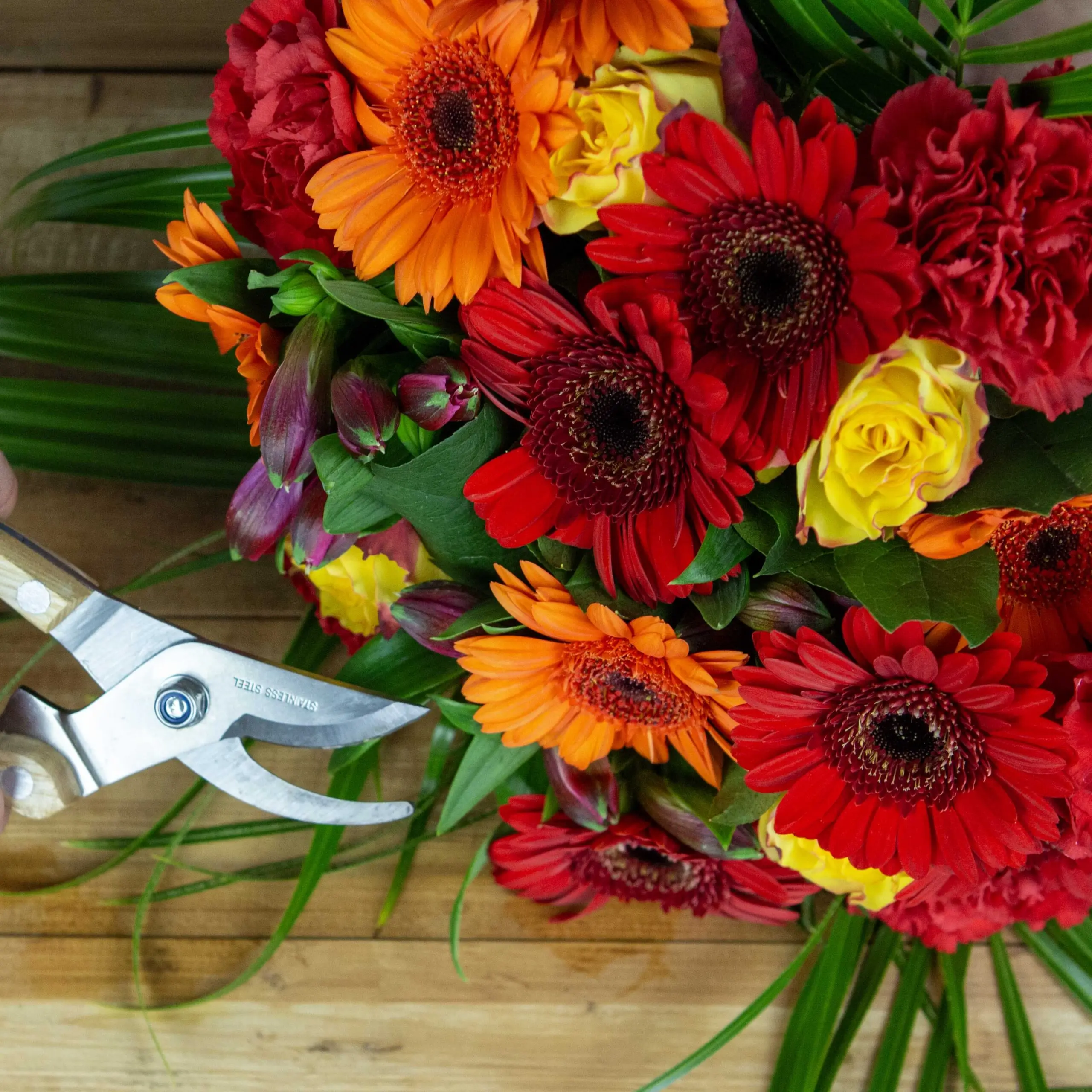 bouquet éclat de germinis, germinis rouge orange et roses jaune avec feuillage tropical