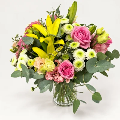 Bouquet à prix canon avec lys jaunes, roses roses et fleurs blanches dans un vase transparent